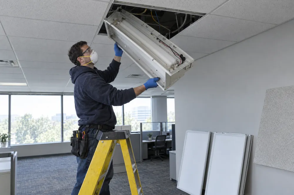 Electrician removing an old fluorescent fixture during a lighting retrofit